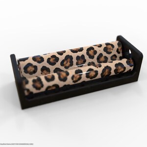 May include: A black rolling tray with a leopard print design. The tray has a rectangular shape with raised edges and a curved roller. The leopard print features brown and black spots on a tan background.