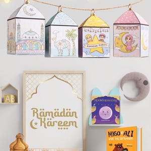 May include: A collection of Ramadan-themed decorations, including paper lanterns, a framed sign with gold lettering, and children's books. The lanterns are shaped like houses and feature illustrations of mosques, camels, and children. The sign reads "Ramadan Kareem."