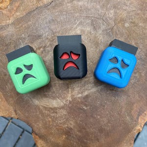 Könnte beinhalten: Drei kleine, 3D-gedruckte Geisterboxen mit traurigen Gesichtern. Die Boxen sind grün, schwarz und blau.