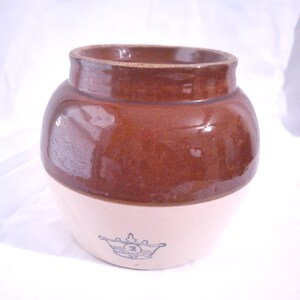 May include: A two-tone stoneware crock with a brown glazed top and a cream base. It has a crown emblem with the number 2. This vintage kitchenware item is likely used for food storage.
