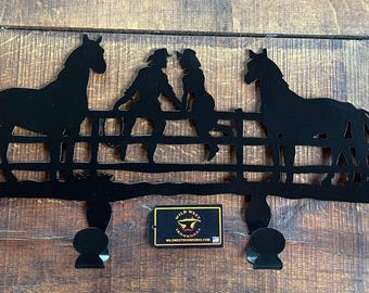 May include: Black metal wall hook with three hooks shaped like horseshoes. The hook features a silhouette of two people riding horses over a fence. The text "Wild West Ironworks" is visible on a small tag.