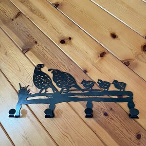 May include: Black metal wall-mounted coat rack with five hooks shaped like a family of quail. The quail are perched on a branch with leaves.