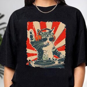 A black t-shirt with a graphic design depicting a cat wearing headphones and playing a turntable, with a red and white sunburst background.