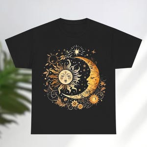 May include: Black t-shirt with a gold sun and moon design. The sun and moon are surrounded by stars and floral elements.