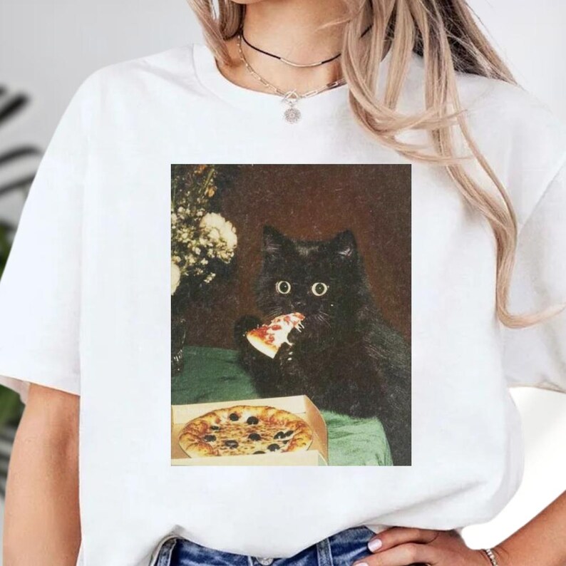 A black cat is sitting on a table, eating a slice of pizza.