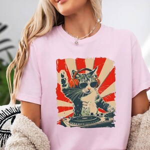 A woman wearing a pink t-shirt with a graphic of a cat playing a DJ turntable.