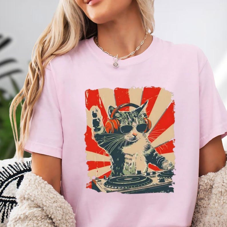 A woman wearing a pink t-shirt with a graphic of a cat playing a DJ turntable.