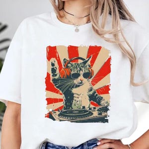 A white t-shirt with a graphic design depicting a cat wearing sunglasses and a turntable, giving the impression of DJing.