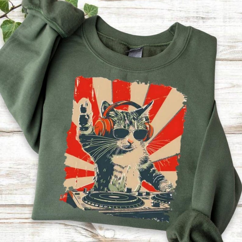 A green sweatshirt with a graphic design depicting a cat wearing sunglasses and headphones, appearing to be playing a musical instrument, such as a drum or guitar.
