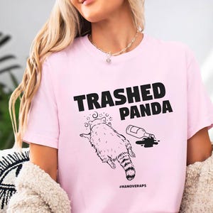 A woman wearing a pink t-shirt with a graphic design and text printed on it.