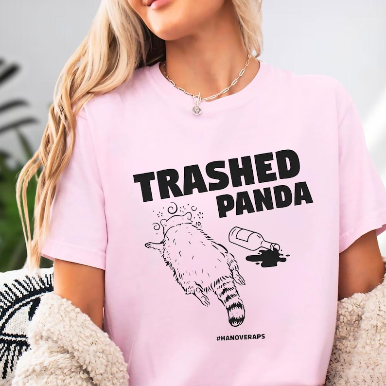 A woman wearing a pink t-shirt with a graphic design and text printed on it.