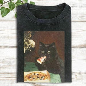 A black cat is sitting on a table, eating a slice of pizza.