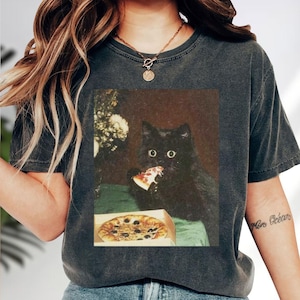 A black cat is sitting on a table, eating a slice of pizza.