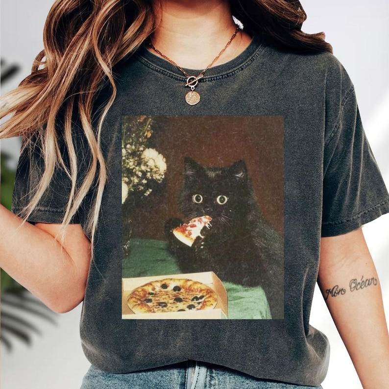 A black cat is sitting on a table, eating a slice of pizza.