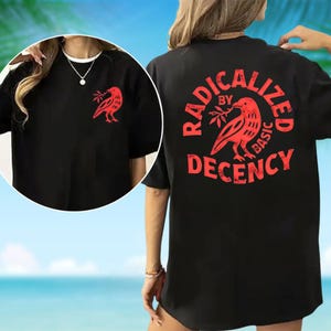May include: Black t-shirt with a red graphic of a bird holding a branch on the front and back. The back of the shirt features the text "RADICALIZED BY BASIC DECENCY" in a circular design around the bird graphic.