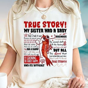 May include: Cream-colored t-shirt with a red graphic and text. The graphic is of a shrimp with large eyes and text that reads "TRUE STORY! MY SISTER HAD A BABY" and more. The shirt has short sleeves.