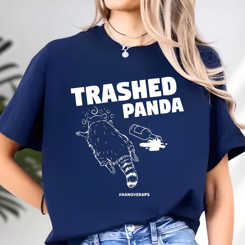A woman wearing a navy blue t-shirt with a graphic design that says "Trashed Panda" and features a raccoon.