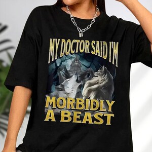 a black t-shirt with a graphic design depicting three wolves and the text "MY DOCTOR SAID I'M MORBIDLY A BEAST" printed on it.