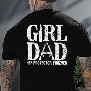 May include: Black t-shirt with the words "GIRL DAD" in distressed white lettering. An image of a rifle is in the center of the word "DAD". The text "HER PROTECTOR, FOREVER" is below the words "GIRL DAD".