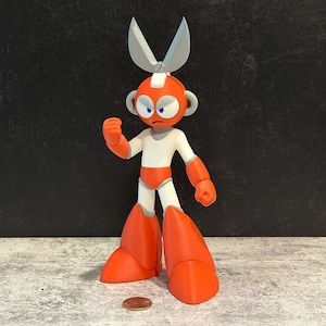 May include: A 3D-printed action figure of a robot character with orange, white, and gray colors. The robot has a scissor-like headpiece and is posed with a clenched fist. A penny is on the surface in front of the figure.