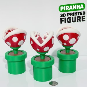 May include: Three 3D-printed Piranha Plant figures from the Super Mario video game series. Each plant has a red head with white spots and a white-lined mouth, set in a green pipe. The text "Piranha 3D Printed Figure" is above the plants.