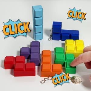 May include: A set of colorful Tetris-shaped blocks with a keychain attached to one of the blocks. The blocks are red, orange, green, yellow, purple, and blue. The keychain has a tag that says "CLICK".