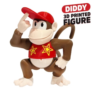 May include: A brown monkey figure wearing a red cap and a red shirt with two yellow star designs. The figure has light-colored hands, feet, and face, and a long tail. Text on the image reads DIDDY 3D PRINTED FIGURE in red and black letters.