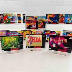 May include: A collection of vintage Super Nintendo game cartridges displayed on clear acrylic stands. The cartridges include Secret of Mana, The Legend of Zelda: A Link to the Past, and Final Fantasy III.