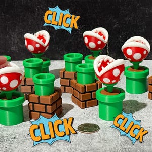 May include: A collection of 3D-printed Piranha Plants from the Super Mario video game series. Each plant features a red and white spotted head with a white interior, set in a green pipe or on a brick base. "CLICK" speech bubbles are also present.
