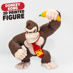 May include: A 3D printed figure of Donkey Kong with brown fur, a light-colored chest, and a red tie featuring the yellow letters DK. The figure is holding a yellow banana with a green tip. Text above the figure reads DONKEY KONG 3D PRINTED FIGURE.