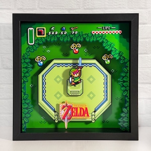 May include: A black framed 3D shadow box with a green background featuring a pixelated image of Link from The Legend of Zelda: A Link to the Past video game. The image includes the game's title card and a heart meter.