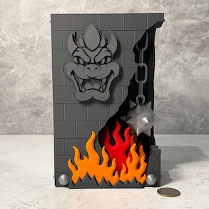 May include: A gray brick wall with a Bowser face, flames, and a spiked ball on a chain. The design is 3D printed and features a black opening with a chain and spiked ball. The flames are orange and red.