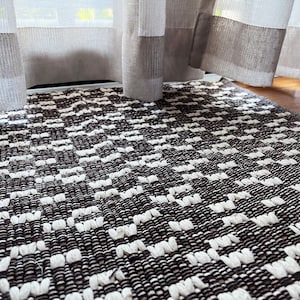 Puede incluir: Una alfombra tejida en blanco y negro con un patrón geométrico. La alfombra está hecha de hilo grueso y texturizado y tiene un diseño moderno y minimalista.