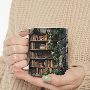 May include: A white ceramic mug with a design of a bookshelf filled with books and vines growing around it. The bookshelf is built into a stone wall.