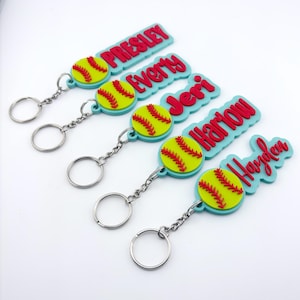 May include: Softball-themed keychains with personalized names in red lettering. Each keychain features a yellow softball with red stitching and a light blue background. The names include Presley, Every, Jeri, Harlow, and Hayden.