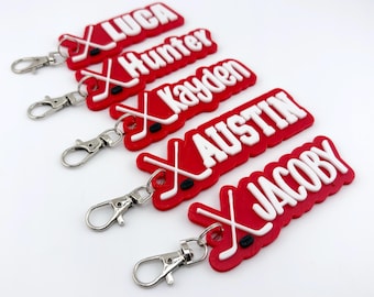 May include: Red hockey-themed keychains with white text spelling out names: Luca, Hunter, Kayden, Austin, and Jacoby. Each keychain features crossed hockey sticks and a black puck. Silver-colored clasps are attached.
