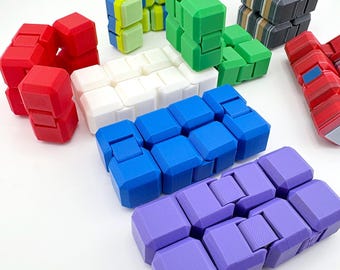 Puede incluir: Una colección de juguetes fidget tipo cubo infinito multicolor en rojo, blanco, azul, verde, morado y un patrón de rayas grises. Cada juguete consta de ocho cubos pequeños conectados que se pueden plegar y manipular en varias formas.