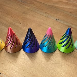 May include: Ten small, cone-shaped decorative objects in various colors, including white, gold, red, blue, green, and purple. Each cone has a textured, fan-like design.