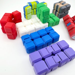 Puede incluir: Una colección de coloridos juguetes fidget en varias formas y colores. Los juguetes son de color rojo, blanco, azul, verde, morado y con un patrón de rayas. Los juguetes están hechos de plástico y están diseñados para ser manipulados y jugados.