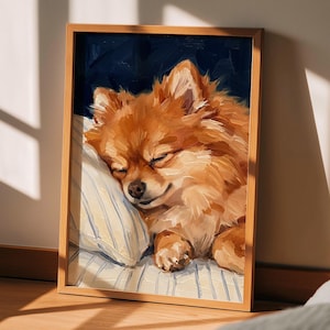 Pode incluir: Uma obra de arte emoldurada retrata um cão da raça Pomerânia a dormir. O cão, com pelo laranja fofo, descansa sobre uma almofada listrada contra um fundo azul escuro. A obra de arte está numa moldura de madeira e a cena é iluminada pela luz do sol.