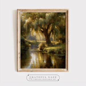 Puede incluir: Pintura de paisaje enmarcada que representa un gran sauce llorón junto a un río tranquilo. La obra de arte presenta tonos cálidos y dorados e iluminación suave, con el reflejo del árbol en el agua. El marco es de madera clara natural. El texto "GRATEFUL GAZE" está en la parte inferior.
