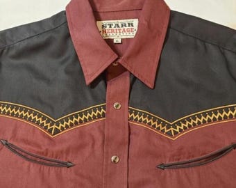 May include: A long-sleeve button-down shirt featuring a maroon and black color-blocked design. The shirt has a pointed collar, a front placket with metallic buttons, and a decorative yellow zigzag pattern across the chest. A label reads Starr Heritage Collection XL.