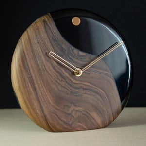 May include: A round wooden and black resin clock with gold hands. The wood has a dark brown grain pattern.