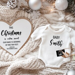 May include: A white heart-shaped sign with the text "This Christmas is extra sweet. Our family is growing by two tiny feet! Arriving December 20XX". A white baby onesie with the text "Baby Smith" and a small ultrasound image.