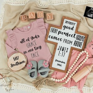 Puede incluir: Un body rosa para bebé con el texto "all of God's GRACE in one tiny FACE" en él. Un crucifijo de madera con el texto "EVERY good and perfect GIFT comes FROM ABOVE JAMES 1:17 December 20XX" está en el fondo. También hay zapatos de bebé, un conejito de madera y un collar de cuentas de madera.