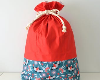 May include: A red drawstring bag with a teal patterned bottom. The pattern features white and gray creatures with red hats, along with red and pink floral accents. The bag is tied with a cream-colored rope.