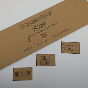 May include: A kraft paper card with the text "SEIT 50 JAHREN L&Ouml;FFELT IHR DIE SUPPE gemeinsam AUS. Alles Liebe zum Hochzeitstag." Three small rectangular cards read "ALLES LIEBE", "GOLDENE HOCHZEIT", and "50".
