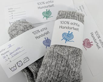 Op de afbeelding: Grijze gebreide sokken met een wit etiket met de tekst "100% echte Handarbeit" en een garenbollogo. De sokken zijn maat 38, gemaakt van 95% katoen en 5% elastaan. Het etiket bevat ook wasvoorschriften.