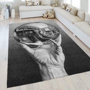 May include: A rectangular area rug featuring a black and white illustration of a large hand holding a reflective sphere. Inside the sphere is a distorted, detailed scene of a person sitting in a room with bookshelves, furniture, and windows.