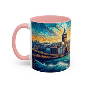Puede incluir: Una taza de cer&aacute;mica blanca con interior rosa, que presenta una imagen de estilo mosaico de una ciudad con una torre alta y una masa de agua. La imagen es vibrante y colorida, con tonos de azul, amarillo, naranja y verde.